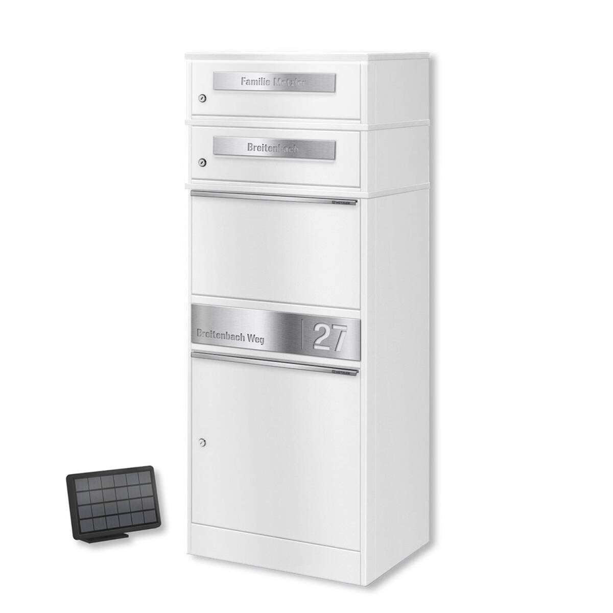 White multi-compartment mailbox unit with metal address plates and a separate small solar panel placed on the floor nearby.