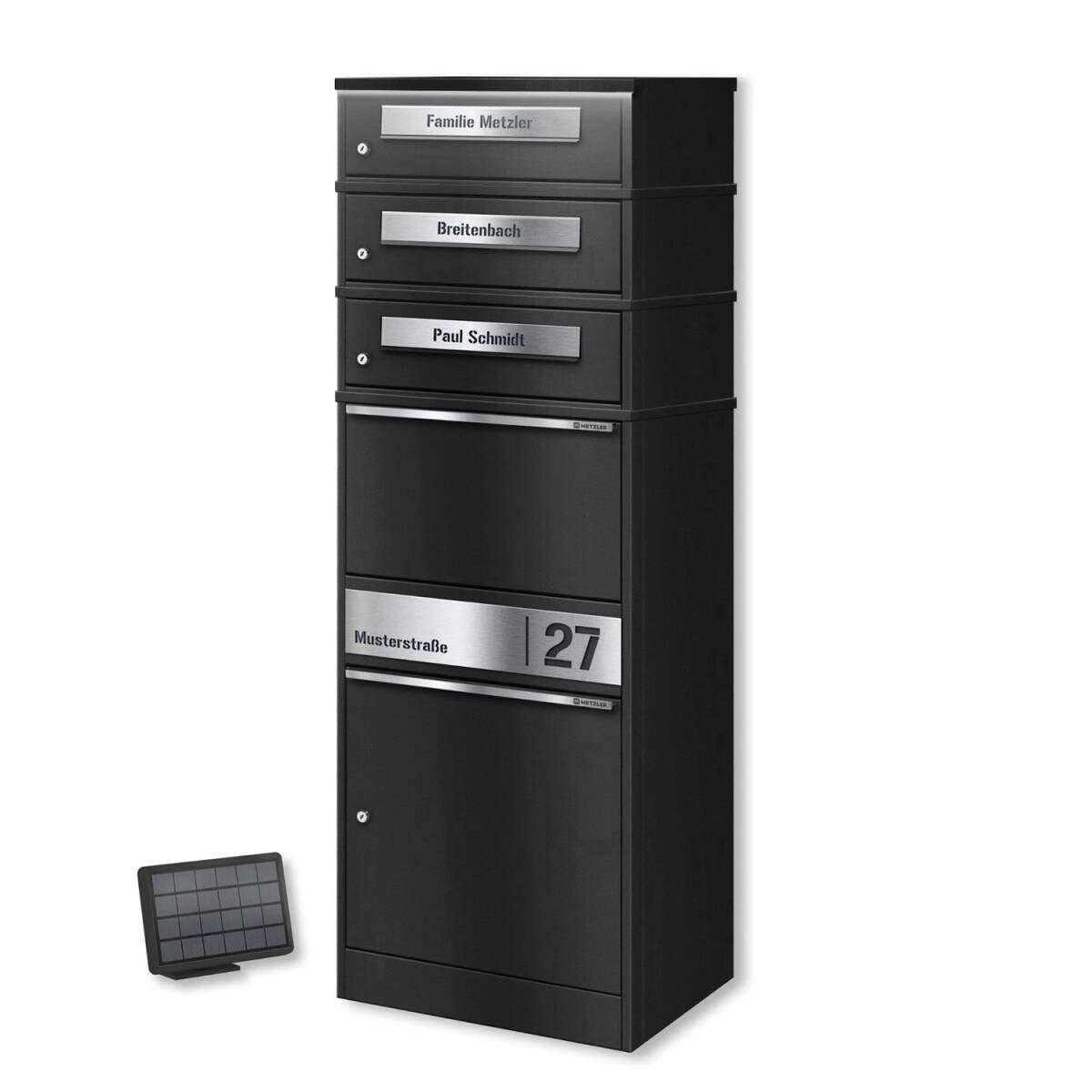 Tall black multi-drawer mailbox with silver nameplates on each compartment and a silver address panel reading 'Musterstraße 27', plus a small solar panel accessory nearby