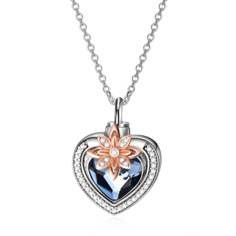 Heart-shaped pendant necklace with a blue gemstone and a diamond-studded border, topped by a rose-gold floral accent.
