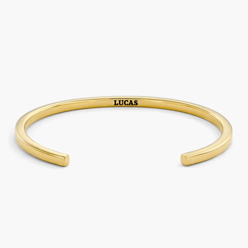 Gold-toned open cuff bracelet with 'LUCAS' engraved on the inner side.