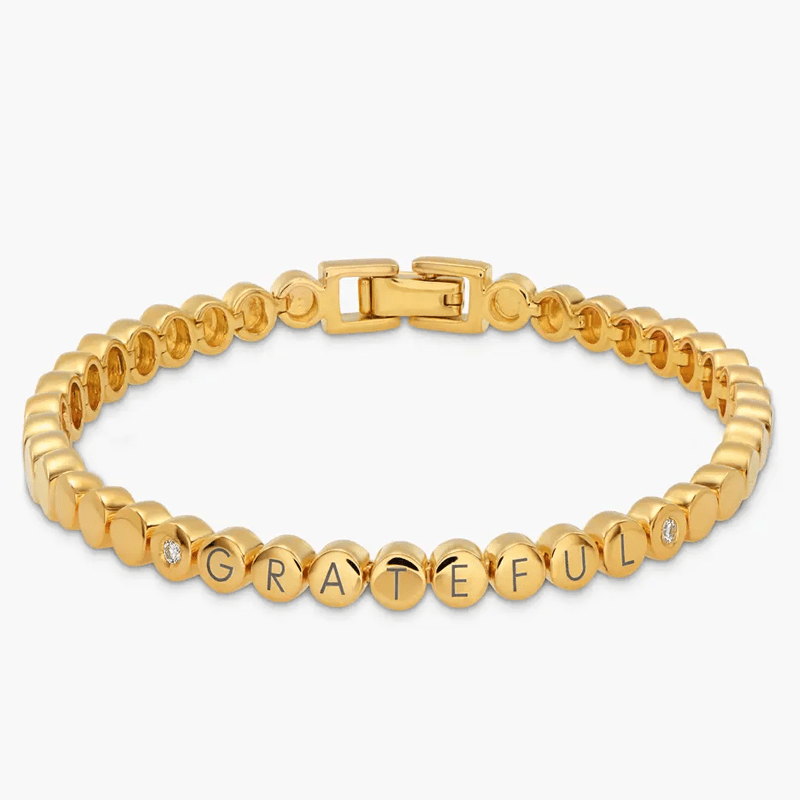 Gold tone bead bracelet spelling 'GRATEFUL' with diamond-accent beads and a secure clasp in the center (jewelry product).
